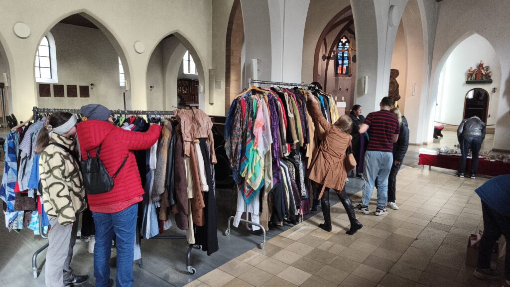 Kleiderstangen mit Kleidung aus dem Martinsladen der Caritas. Menschen, die sich die Kleidung anschauen