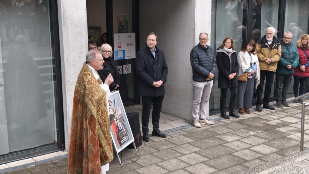 Dekan Martin Heim spricht vor dem Martinsladen Segnungswünsche, Mitarbeiter*innen der Caritas stehen dabei.
