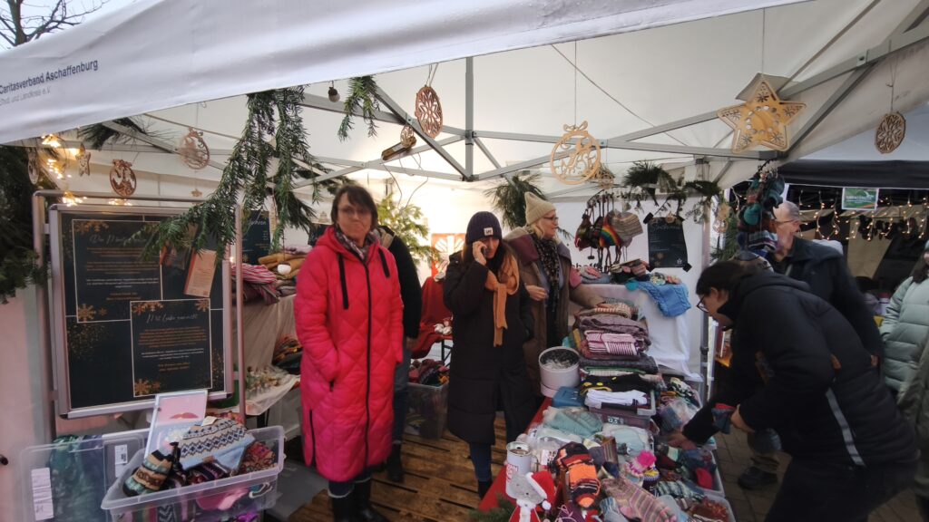 Kund*innen stöbern am Stand der Caritas in den angebotenen Strickwaren: Decken, Mützen und Handschuhe.